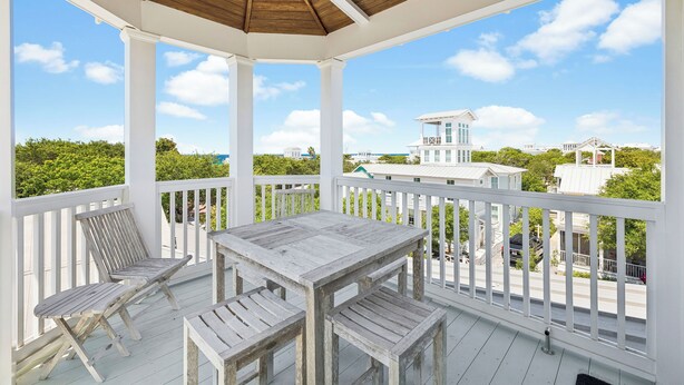 Eine überdachte Veranda mit Tisch und Stühlen, weißen Geländern und Blick auf die umliegenden Gebäude.
