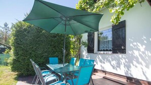 Un patio al aire libre con una mesa, sillas, un paraguas verde y un edificio blanco con una ventana.