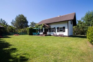 A single-story house with a tiled roof, a small porch with a bench, and a grassy yard. - Holiday Villa With Private Garden, Lubiatowo (Choczewo)