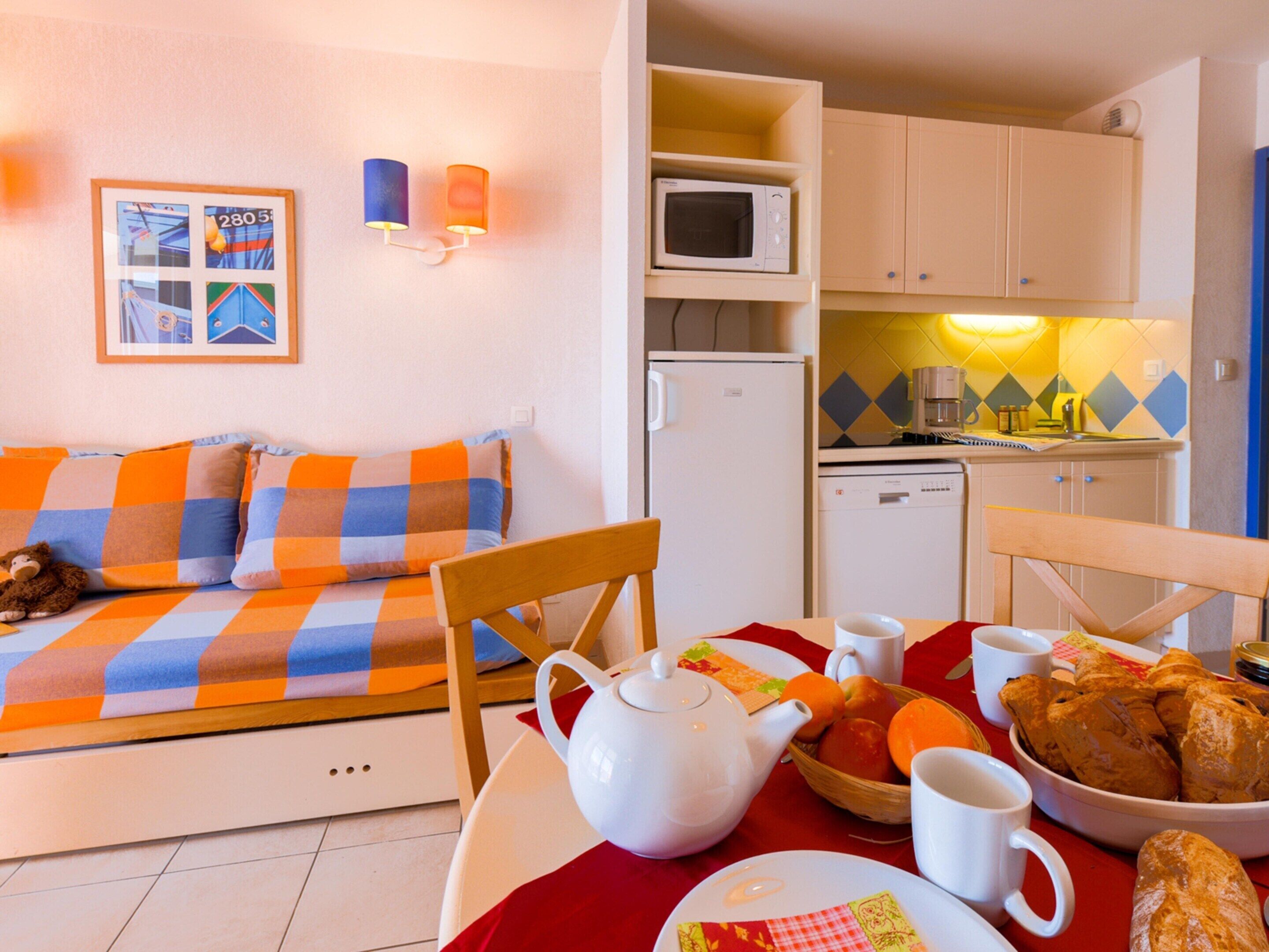 Une pièce chaleureuse avec un canapé à carreaux, une table à manger avec une théière, un four à micro-ondes et un petit coin cuisine.