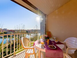 A balcony with a table set for two, overlooking a body of water and buildings.
