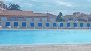 Una piscina con sillas azules, techo de azulejos y edificios al fondo.
