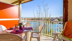 Un balcón con mesa lista para comer, sillas y vista al mar y edificios.