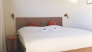 Un lit bien fait, avec une couette blanche, deux oreillers et des serviettes pliées, le tout posé sur une tête de lit en bois.