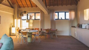 Une pièce chaleureuse avec un plafond en bois, un coin repas avec des chaises et une table, un coin cuisine et de grandes fenêtres.