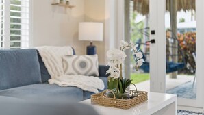 Uma sala de estar com um sofá azul, uma mesa de centro branca com um cesto trançado e uma orquídea em vaso.
