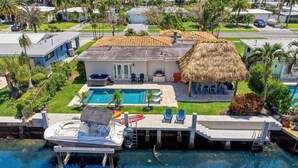 Uma casa com piscina, um barco atracado no cais e uma construção com telhado de palha.