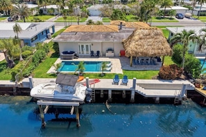 Ein Haus mit Swimmingpool, ein Boot an einem Steg und ein Gebäude mit Strohdach.
