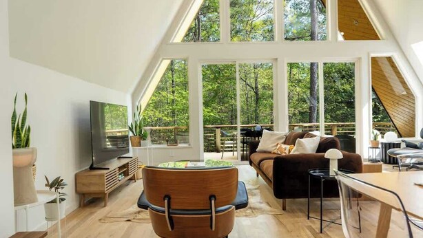 Ein geräumiges Loft mit großem Fernseher, Holzmöbeln und Blick auf den Wald durch große Fenster.