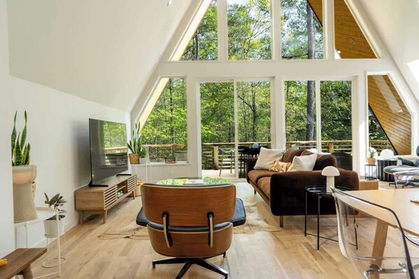 Ein geräumiges Loft mit großem Fernseher, Holzmöbeln und Blick auf den Wald durch große Fenster.
