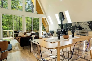 Ein modernes Interieur mit Essbereich, Küche und großen Fenstern mit Blick auf einen Wald.