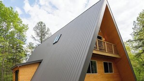 Ein modernes A-Haus mit geneigtem Dach, Holzfassade und kleiner Veranda.
