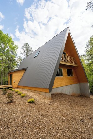 Ein modernes A-Haus mit geneigtem Dach, Holzfassade und kleiner Veranda.