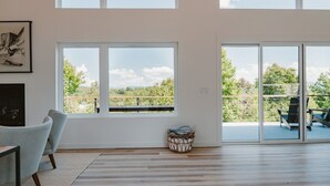 A spacious room with large windows, a fireplace, and a view of greenery. - The Perch | Poolside Modern Mountain Retreat (Young Harris)