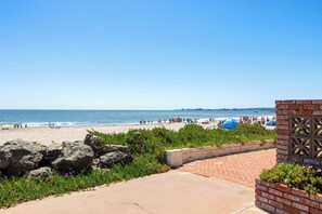 Vista de platja amb un passeig pavimentat, una paret de maó i una reixa decorativa.