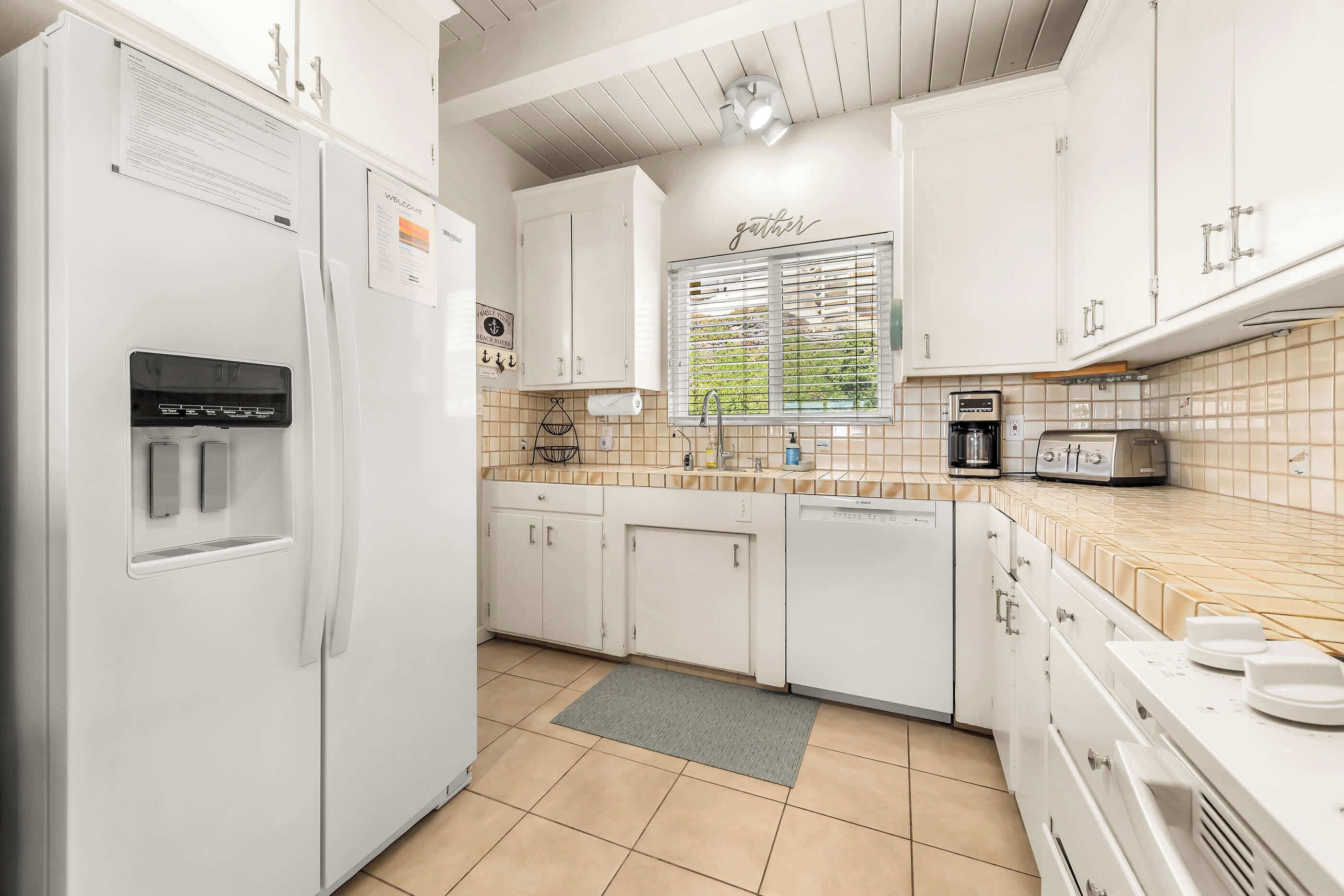 Una cocina con armarios blancos, un refrigerador empotrado, una cafetera y un tostador.