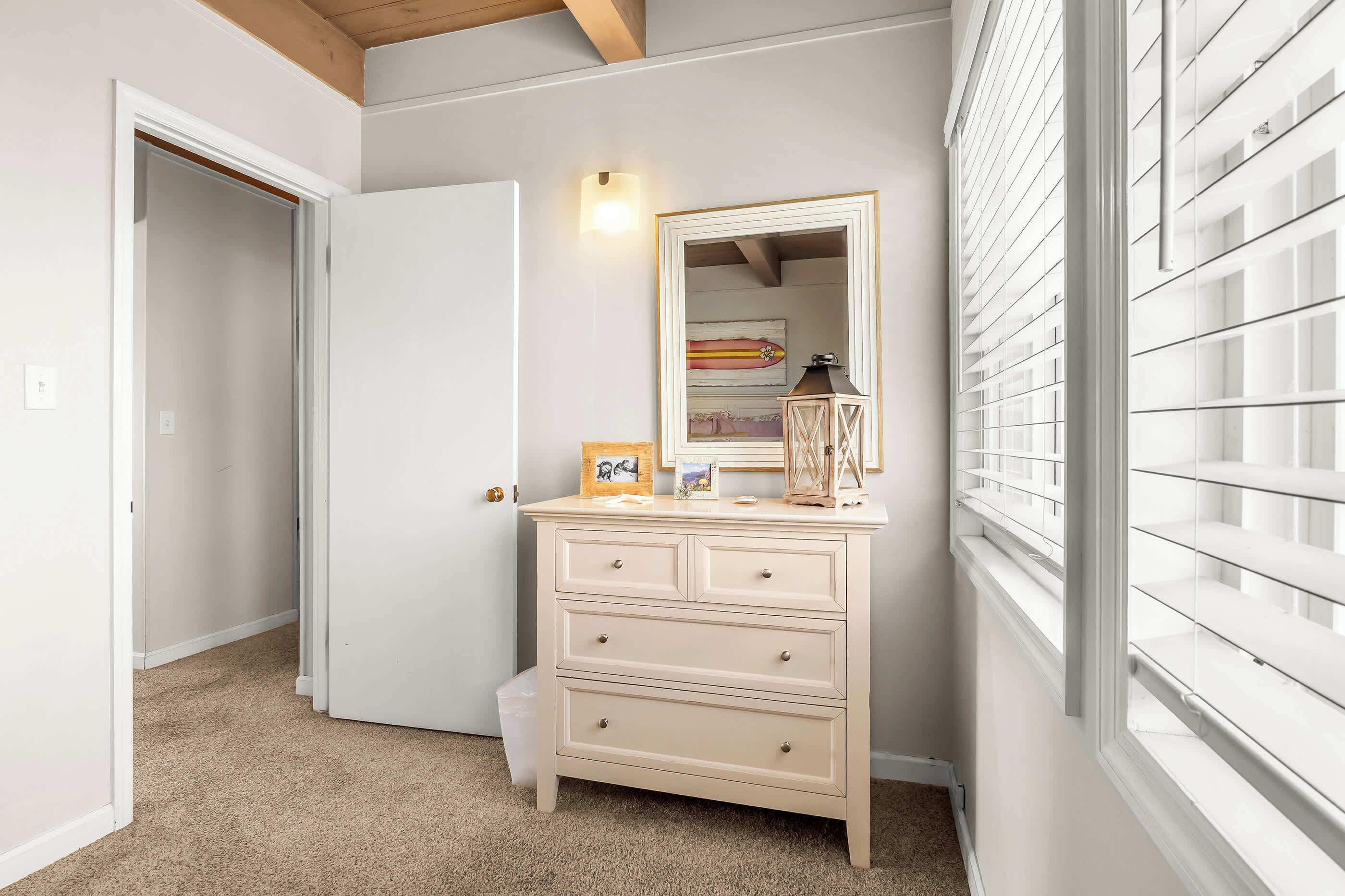 A hallway with a beige dresser, a mirror, and a window with blinds.