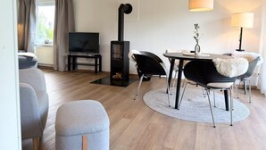 Een moderne woonkamer met een open haard, een televisie, een eettafel met stoelen en een bank.