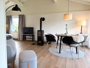 Ein modernes Wohnzimmer mit Kamin, Fernseher, Esstisch mit Stühlen und einer Couch.