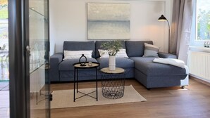 Een moderne woonkamer met een hoekbank, een ronde salontafel, een vloerlamp en een groot abstract schilderij aan de muur.