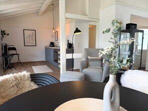 Ein modernes Wohnzimmer mit Esstisch, grauen Sesseln, einer schwarzen Lampe und einer Vase mit Blumen.