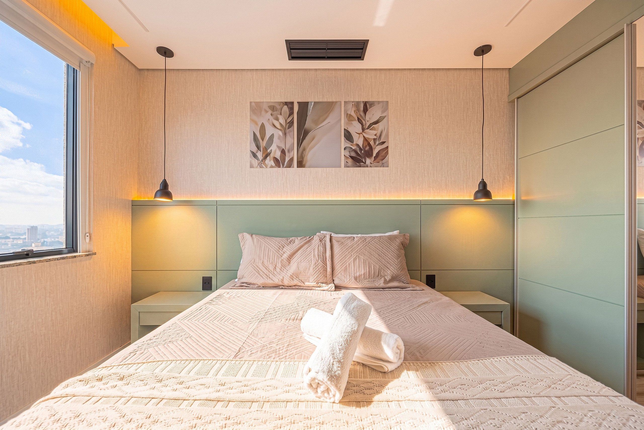 Quarto de hotel com uma cama, duas mesas de cabeceira, uma janela e vista para a cidade.