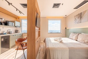 A compact hotel room with a kitchenette, a bed with a view, and a dining area. - Hospedez - Flat Premium Osasco Trade (Osasco)