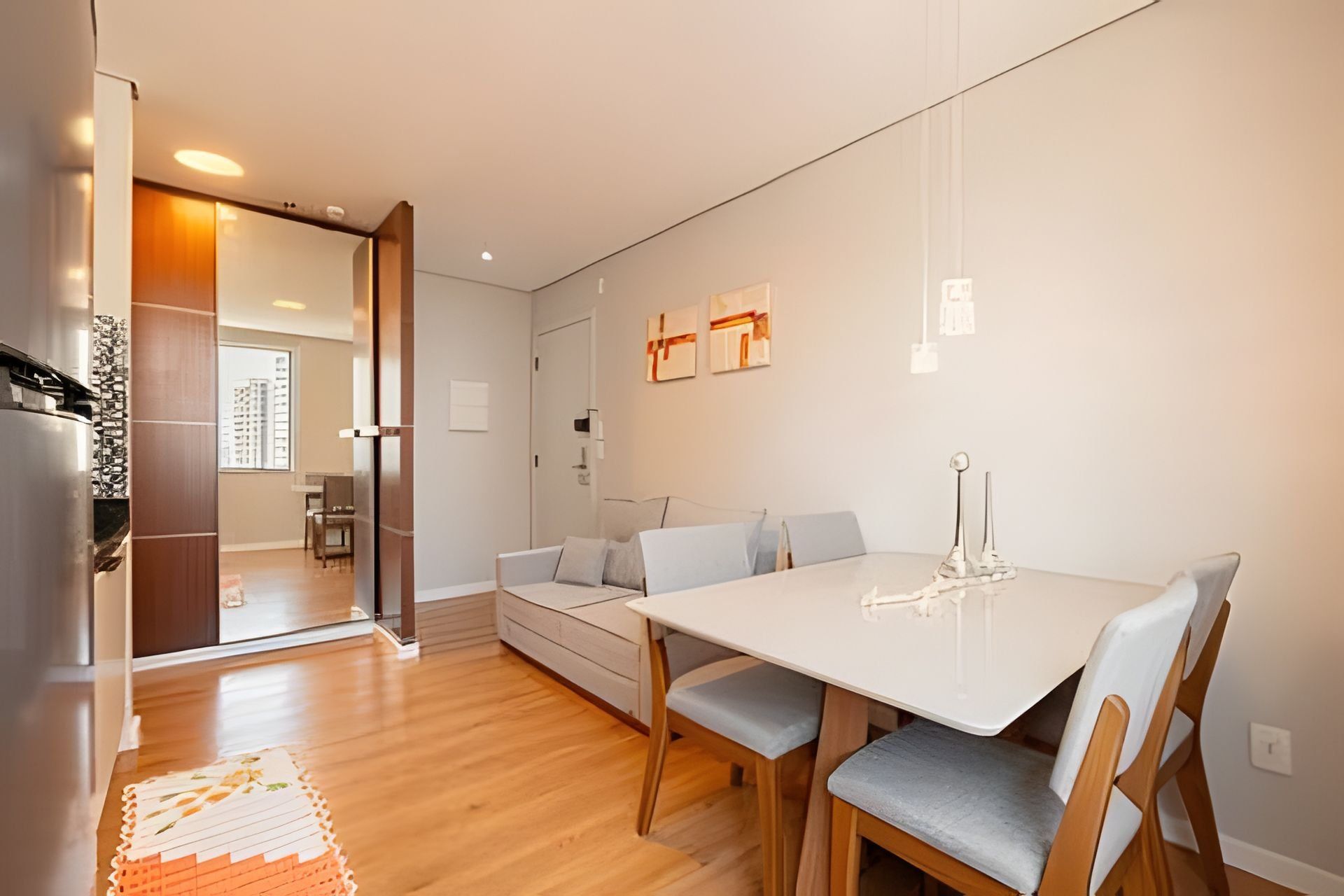 A modern living space with a dining area, a sofa, and a kitchen visible through an open door.