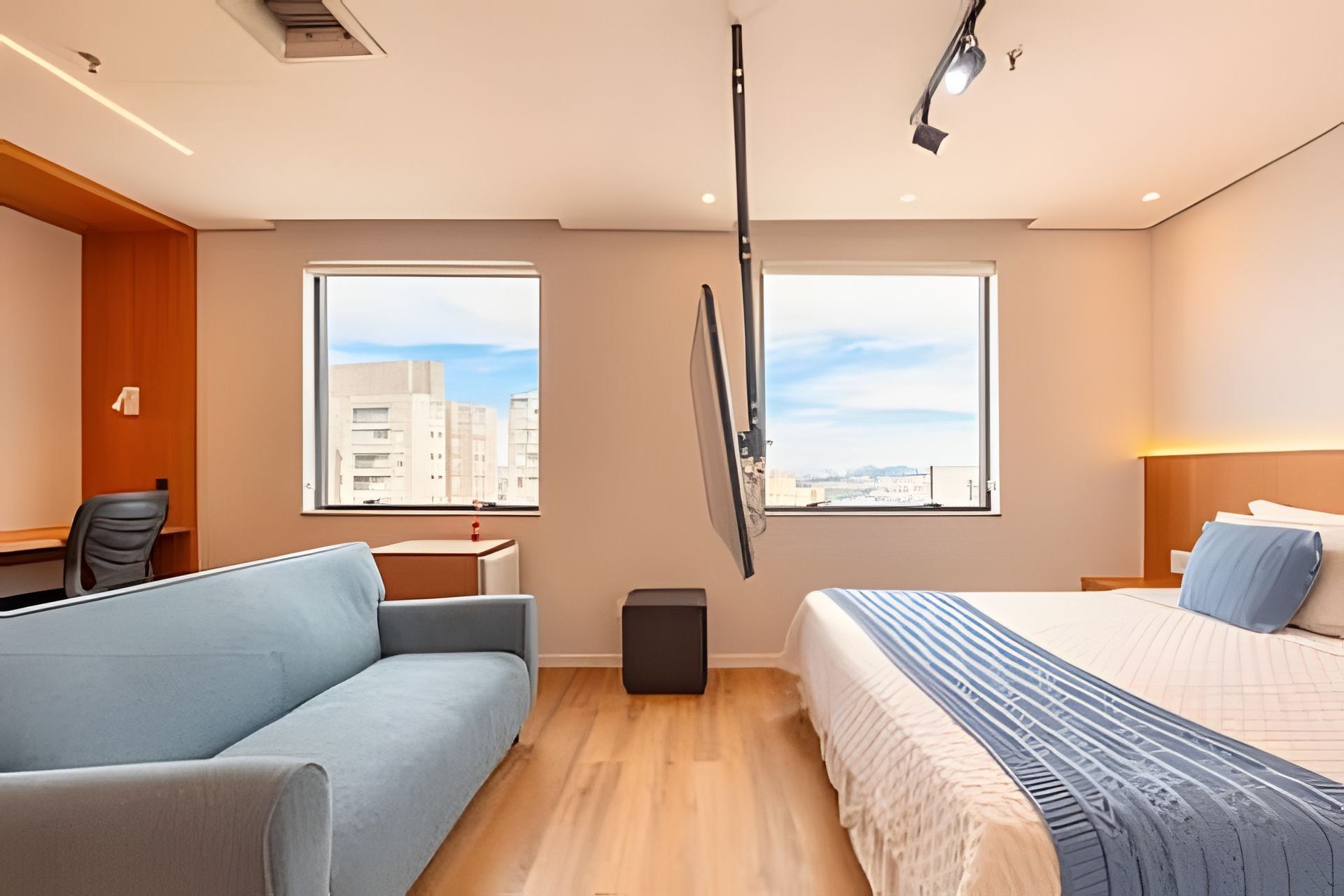 Habitación de hotel moderna con sofá, cama, escritorio y dos ventanas con vistas a la ciudad.