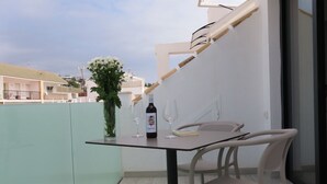 Ein Balkon mit Tisch, Stühlen, einer Weinflasche und einem Buch.