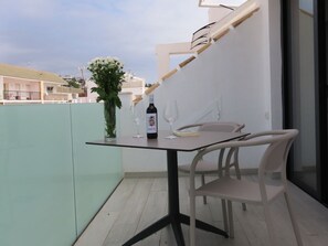 Ein Balkon mit Tisch, Stühlen, einer Weinflasche und einem Buch.