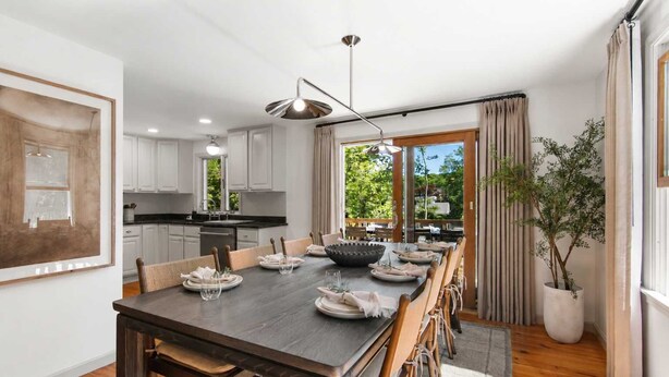Une cuisine moderne avec des meubles blancs, un coin repas doté d’une table en bois foncé, et une vue sur la verdure à l’extérieur.