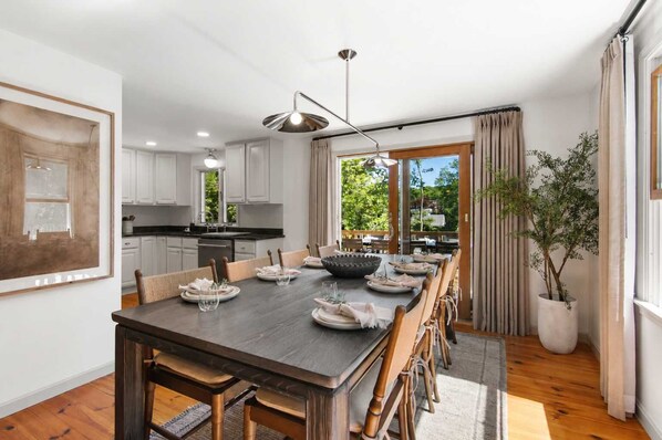 A modern kitchen with white cabinets, a dining area with a dark wooden table, and a view of greenery outside. - 1 Mile to Campground Beach, Dog Friendly, AC! (Eastham)