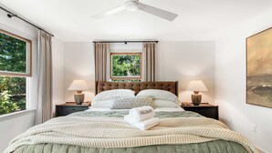 Un lit bien fait, recouvert d’une couvre-lit verte, avec deux lampes de chevet, un ventilateur de plafond et une fenêtre avec des rideaux.