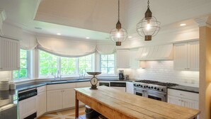 A kitchen with white cabinetry, a wooden table, and hanging pendant lights. - Private Beach, Sweeping Water Views, Game Room! (Brewster)
