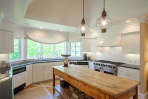 A kitchen with white cabinetry, a wooden table, and hanging pendant lights. - Private Beach, Sweeping Water Views, Game Room! (Brewster)