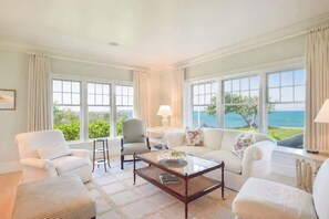 A spacious living room with a large window overlooking a scenic view, a comfortable seating area with a coffee table, and a view of the ocean.