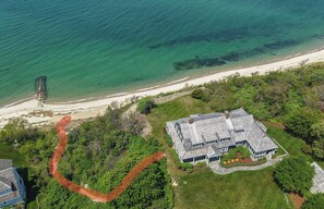An aerial view of a coastal property with a large house, a beach, and a stone structure near the water. - Private Beach, Sweeping Water Views, Game Room! (Brewster)