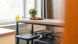 Janela com cortinas de renda, uma planta em vaso sobre uma mesa de madeira e um radiador abaixo.