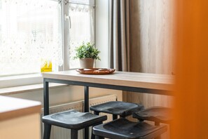 Ein Fenster mit Spitzenvorhängen, ein Blumentopf auf einem Holztisch und ein Heizkörper darunter.