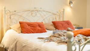 Uma cama com estrutura de metal, duas almofadas, um cobertor e um xale de tricô.