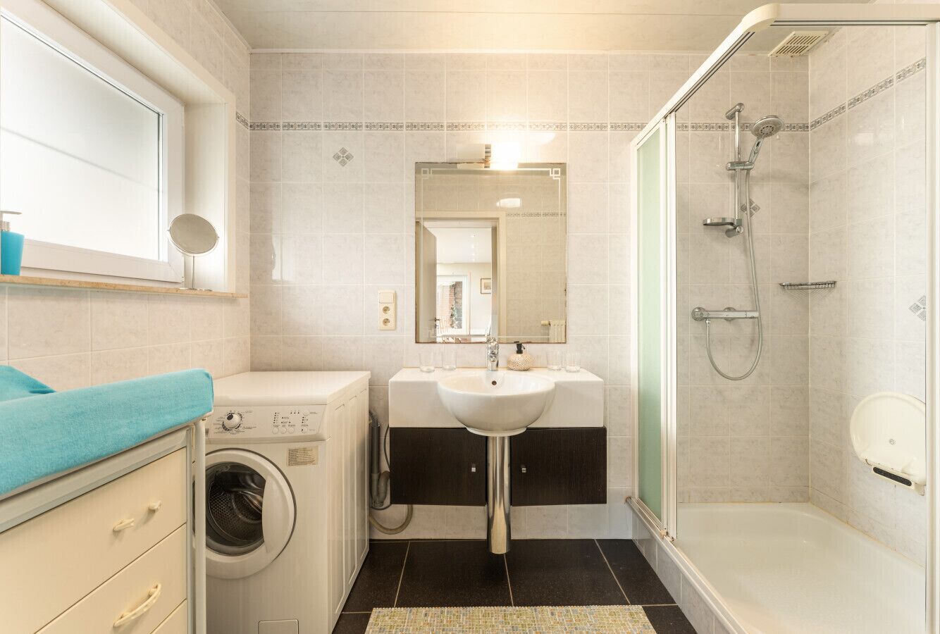 Une salle de bain équipée d’un lave-linge, d’un lavabo, d’un miroir et d’une douche.