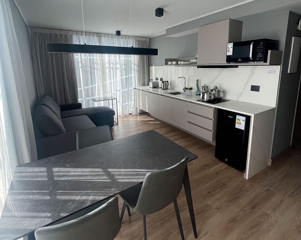 A modern kitchen with a microwave, sink, and cabinets. There is a dining table with chairs and a sofa in the living area.