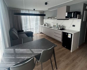 Eine moderne Küche mit Mikrowelle, Spüle und Schränken. Im Wohnbereich befindet sich ein Esstisch mit Stühlen sowie eine Couch.