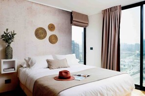 A modern hotel room with a large bed, a city view, a wall with woven decor, and a nightstand with a vase. - Málaga EXC I Chic 1 BR Apartment in El Golf (Santiago)