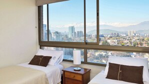 Ein Hotelzimmer mit zwei Betten, einem Nachttisch, einer Lampe und einem großen Fenster mit Blick auf die Stadt.