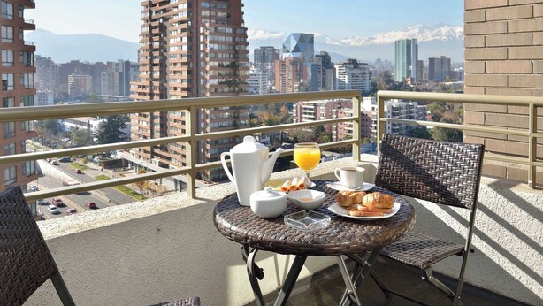 Ein Balkon mit Frühstücksangebot, einem Stuhl und Blick auf eine Stadtlandschaft mit Bergen.
