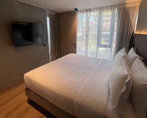 A hotel room with a bed, a flat-screen TV mounted on the wall, and a window with curtains. - One Manquehue EXC | Bright 1BR Apartment (Santiago)
