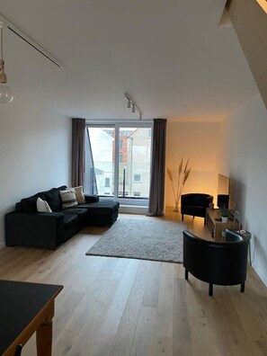 Ein modernes Wohnzimmer mit einem Ecksofa, einem kleinen Tisch und einem schwarzen Sessel.
