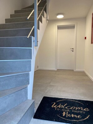 Eine Treppe führt zu einer Tür, vor der eine Fußmatte mit dem Schriftzug 'Welcome to our happy home' liegt.